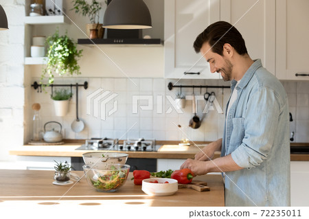 Side view smiling man cutting fresh vegetables, cooking in kitchen 72235011