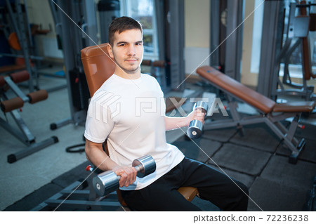 young handsome male has personal workout or exercising with dumbbells in gym young handsome male has personal workout or exercising with dumbbells in gym 72236238