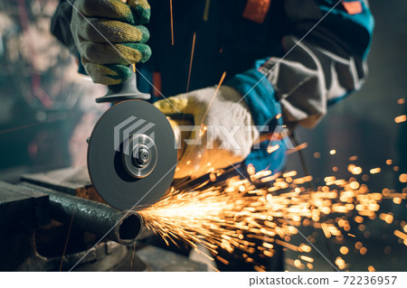 Locksmith in special clothes and goggles works in production. Metal processing with angle grinder. Sparks in metalworking 72236957