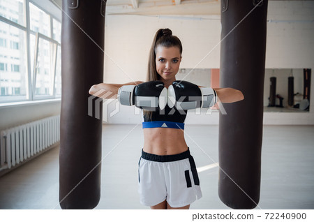Cute girl posing for a photo in boxing gloves on the background of punching bags Cute girl posing for a photo in boxing gloves on the background of punching bags 72240900