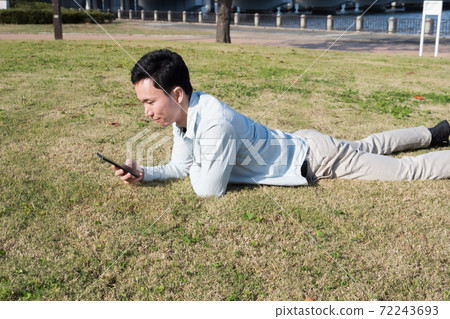 一個人躺在草坪上看著智能手機 一個人躺在草坪上看著智能手機 72243693