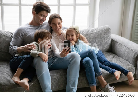 Relaxed young parents using smartphone with kids. Relaxed young parents using smartphone with kids. 72245566