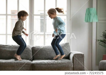 Energetic little kids siblings jumping barefoot on couch. 72245575