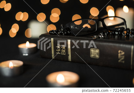 Rosary, glasses on holy bible book and burning candles at night against bokeh light background Rosary, glasses on holy bible book and burning candles at night against bokeh light background 72245655