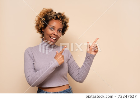 Attractive cheerful african woman with curly hair points aside, shows direction on free space Attractive cheerful african woman with curly hair points aside, shows direction on free space 72247627