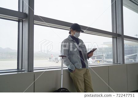young asian man reading e-book using a e-reader while waiting for boarding in terminal building 72247751