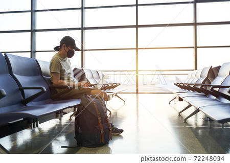asian man male air traveler sitting in airport waiting area using laptop computer 72248034