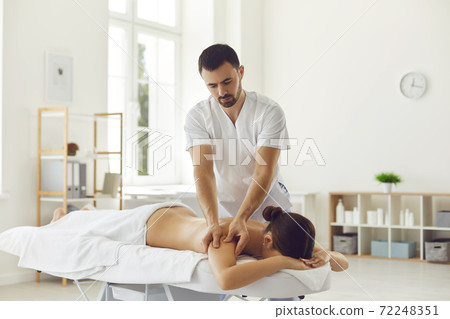 Professional masseur doing therapeutic body massage for young woman lying on massage table 72248351
