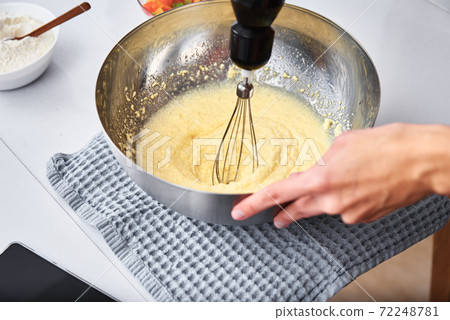 Woman in kitchen cooking a cake. Hands beat the dough with an electric mixer 72248781