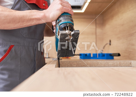 Repairman using electric jigsaw. Sawing place for installing gas hob in worktop Repairman using electric jigsaw. Sawing place for installing gas hob in worktop 72248922