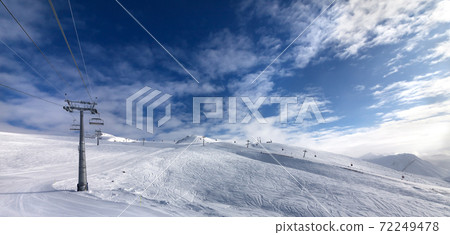 Ski slope, chair-lift on ski resort and blue sky with sunlight clouds Ski slope, chair-lift on ski resort and blue sky with sunlight clouds 72249478