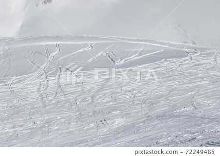 Snowy slope with traces of skis and snowboards 72249485