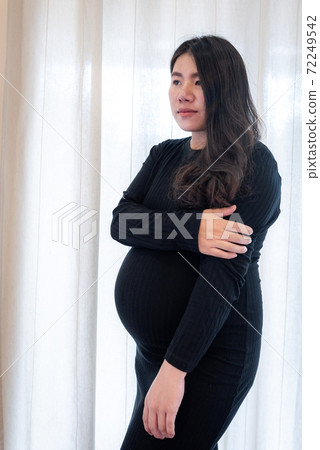 Pretty young pregnant woman standing by the window in room.Concepts of pregnancy and family Pretty young pregnant woman standing by the window in room.Concepts of pregnancy and family 72249542