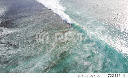 Surfers catch waves at Uluwatu beach, Bali. Huge waves stretch along the beach. Surfers catch waves at Uluwatu beach, Bali. Huge waves stretch along the beach. 72251344