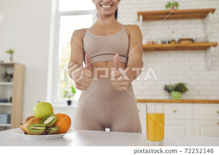 Cropped image of fitness woman in sports uniform showing thumbs up near fruits and fresh juice. Cropped image of fitness woman in sports uniform showing thumbs up near fruits and fresh juice. 72252146