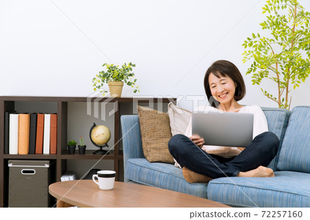 A woman operating a computer on the sofa 72257160