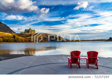 Red chair look over Waterton Lake Marina Point in autumn foliage season sunny morning. Blue sky with colourful clouds reflect on the lake water surface. Waterton Lakes National Park, Alberta, Canada. 72257297