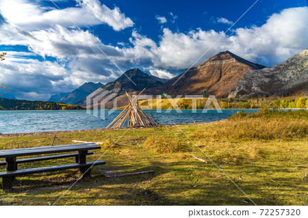 Driftwood Beach, Middle Waterton Lake lakeshore in autumn foliage season morning. Blue sky, white clouds over mountains in the background. Landmarks in Waterton Lakes National Park, Alberta, Canada. 72257320