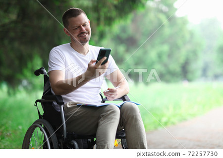 Happy disabled person sit in wheelchair in park and chatting on phone. Happy disabled person sit in wheelchair in park and chatting on phone. 72257730