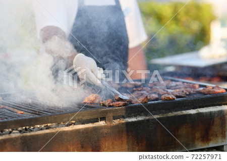 Chef grills cuts of meat on barbeque in smoke outside. Chef grills cuts of meat on barbeque in smoke outside. 72257971