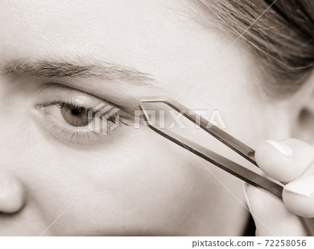 Woman tweezing eyebrows depilating with tweezers 72258056
