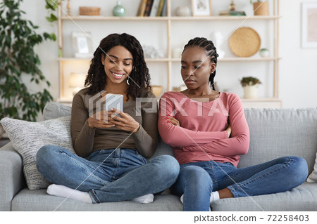 Happy african lady sitting by angry bestie, chatting with lover 72258403