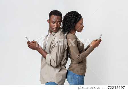 African man and woman standing back to back, using smartphones 72258697