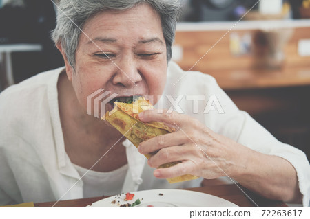 old asian elderly senior elder woman eating vegan wrap with quinoa, black bean, mango, cashew nut, bell pepper 72263617