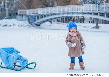 Portrait of a little girl with a sleigh on a background of snow in the park 72266309