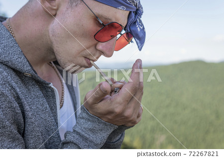 Close-up of young man smoking marijuana joint outdoors Close-up of young man smoking marijuana joint outdoors 72267821