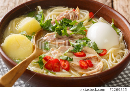 Delicious chicken noodle soup with boiled egg and herbs close-up in a plate. vertical 72269835