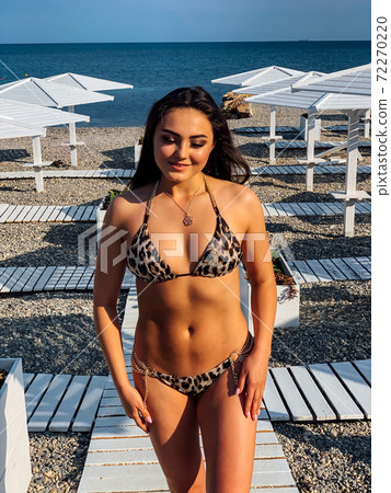 Beautiful brunette woman in swimsuit sunbathes on the beach by the sea Beautiful brunette woman in swimsuit sunbathes on the beach by the sea 72270220