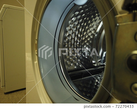 The landromat door is open and we see light inside the radiant metal drum 72270433