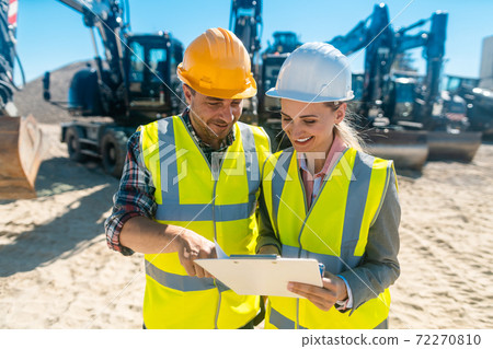 Two workers in open cast mine standing in front of heavy machinery 72270810
