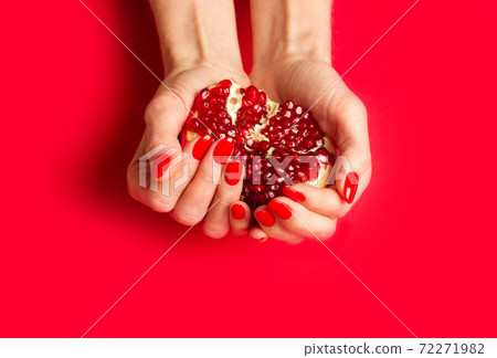 Red fresh pomegranate in woman's hands, fingernails with red nail polish on red background. Red fresh pomegranate in woman's hands, fingernails with red nail polish on red background. 72271982
