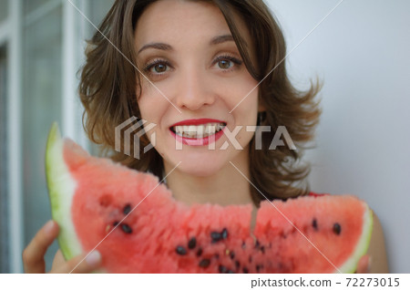 Close up indoors portrait of beautiful woman with short hair and sensual lips eating a piece of watermelon. Hedonism, happiness and buoyancy Close up indoors portrait of beautiful woman with short hair and sensual lips eating a piece of watermelon. Hedonism, happiness and buoyancy 72273015