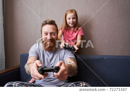Father and his little cute daughter with gamepads Father and his little cute daughter with gamepads 72273387