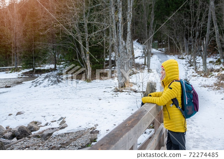 Hiker woman with her backpack and yelloe down jacket stands on mountain trail admires beautiful views. Hiker woman with her backpack and yelloe down jacket stands on mountain trail admires beautiful views. 72274485
