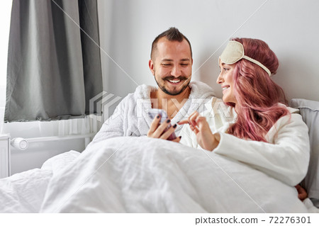 happy couple with smartphones in pajamas on their bed happy couple with smartphones in pajamas on their bed 72276301