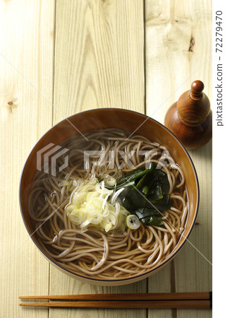 A simple kake soba topped with chopped green onions and wakame seaweed and a gourd-shaped shichimi bowl (overhead view) 72279470