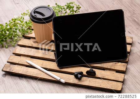 A tablet cofee earphon with drinks, black earphones and a tablet device placed on a wooden desk A tablet cofee earphon with drinks, black earphones and a tablet device placed on a wooden desk 72288525