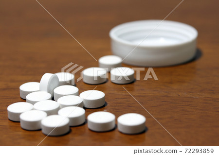 Pile of white round medicine on the wooden floor and white plastic cap. 72293859
