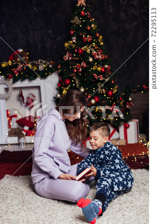 Mom and son read a book at the Christmas tree presents the lights of the garland new year 72295113