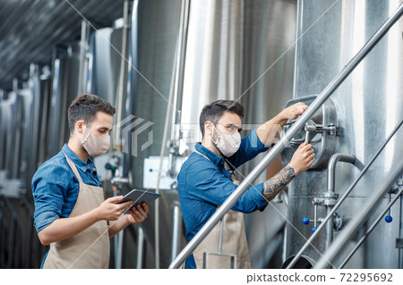 Young attractive workers in aprons and protective masks close vent on kettle 72295692