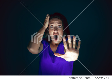 Close up portrait of young crazy scared and shocked woman isolated on dark background Close up portrait of young crazy scared and shocked woman isolated on dark background 72295757