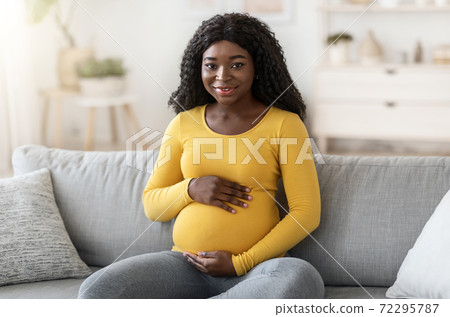 Beautiful black pregnant woman sitting on couch at home 72295787