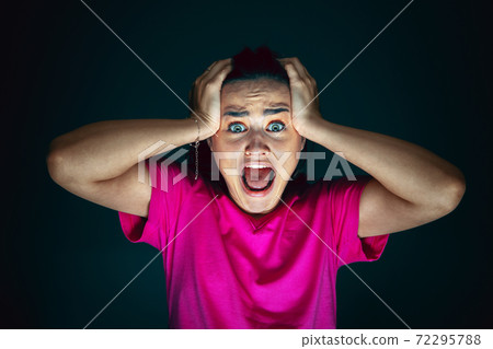 Close up portrait of young crazy scared and shocked woman isolated on dark background 72295788