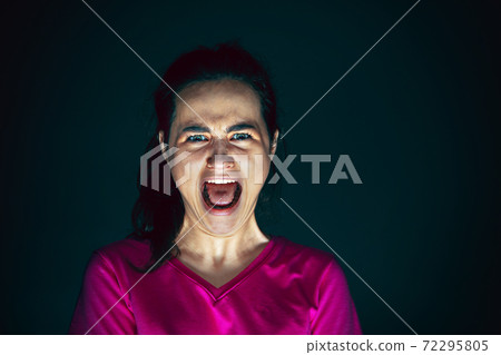 Close up portrait of young crazy scared and shocked woman isolated on dark background 72295805