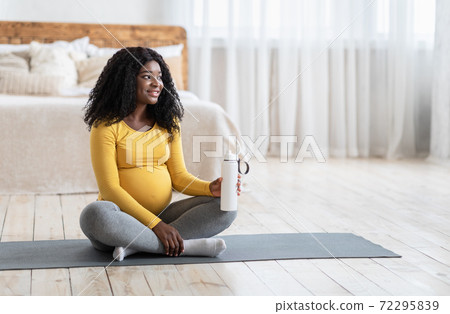 Pregnant african american lady drinking water during exercising 72295839