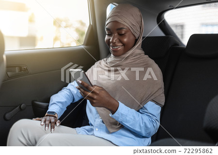 Black muslim business lady in hijab using smartphone while traveling by car 72295862
